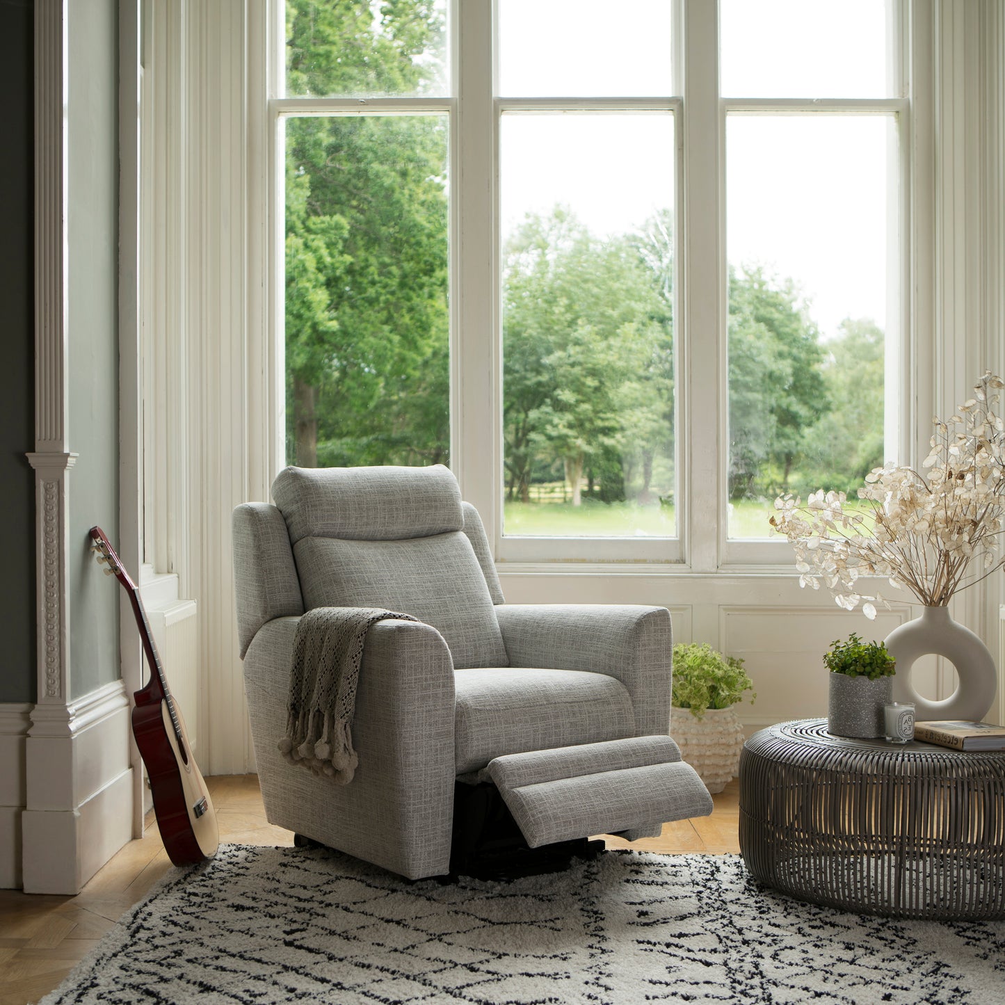 Gray recliner chair in a living room with large windows and decorative elements.