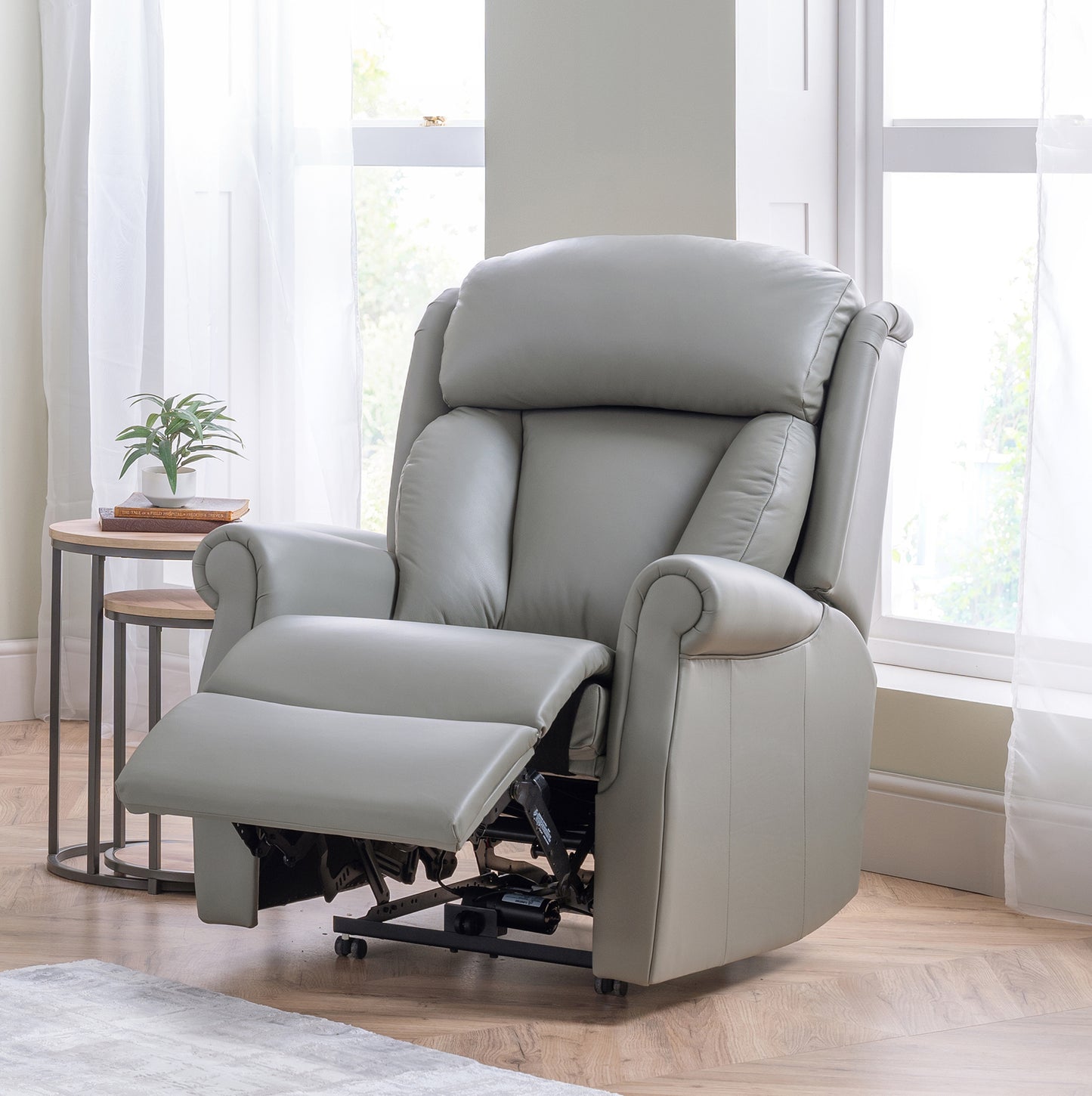 Gray celebrity riser recliner chair in a room with light wood flooring and white curtains.