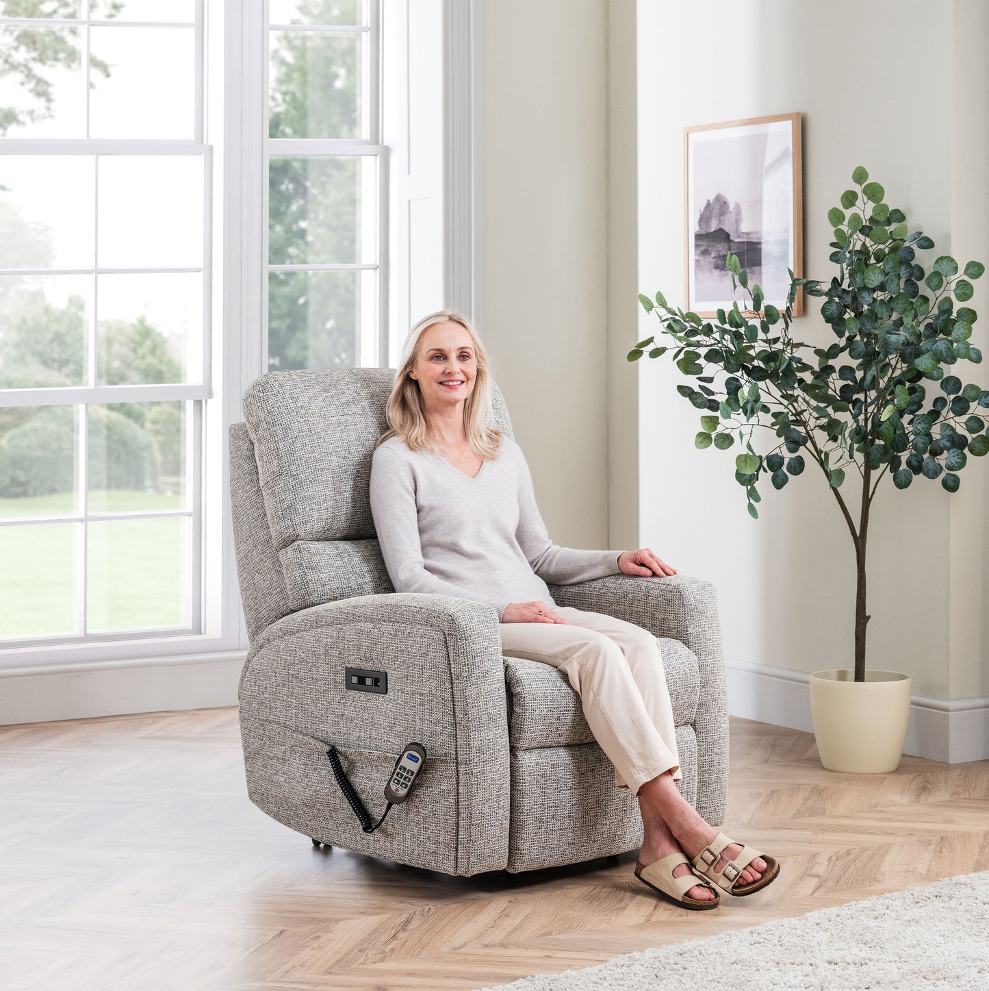 Woman sitting in a Celebrity Southwell recliner chair in a bright living room with a plant and window.