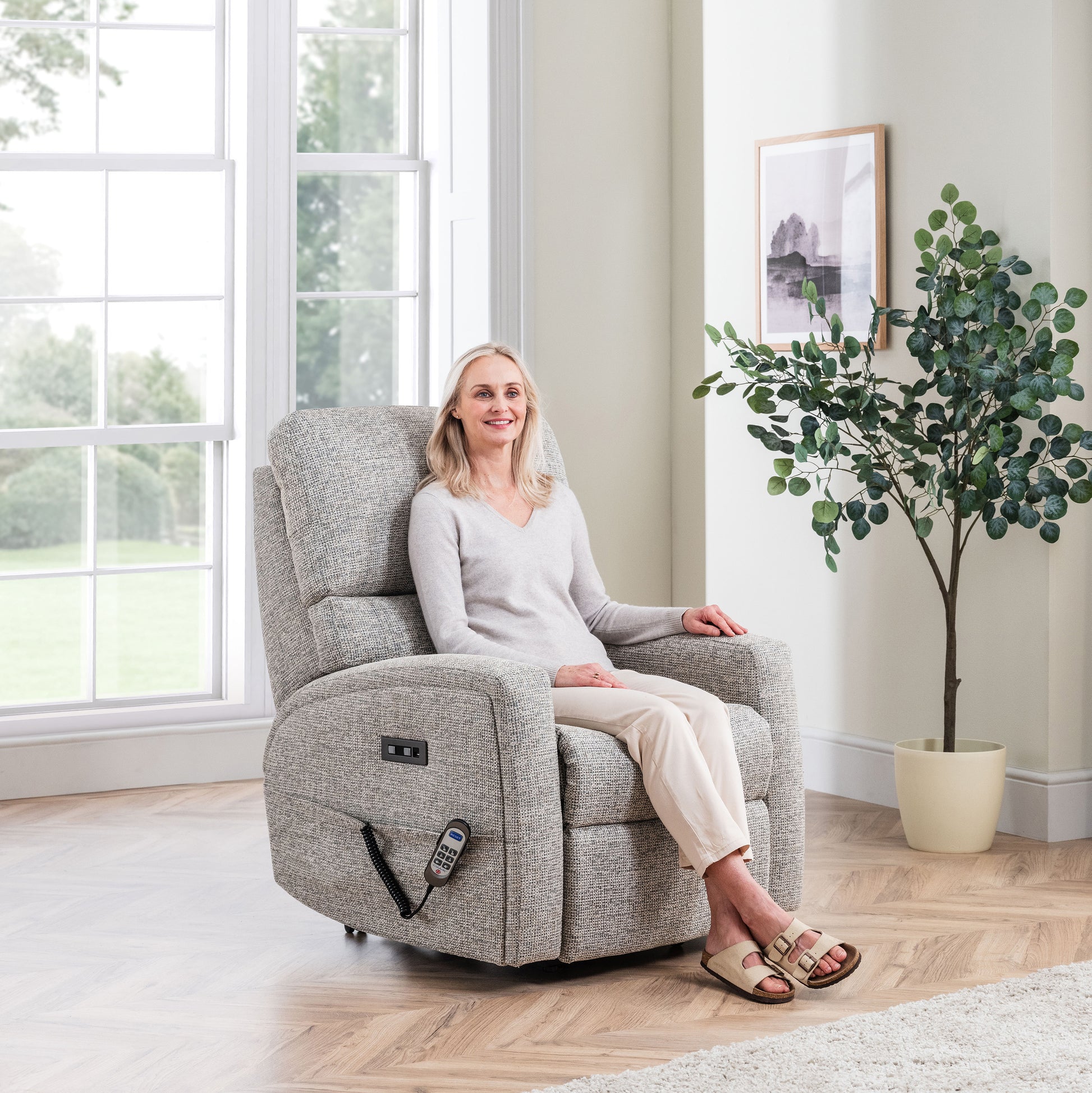 Woman sitting in a Celebrity Southwell recliner chair in a bright living room with a plant and window.