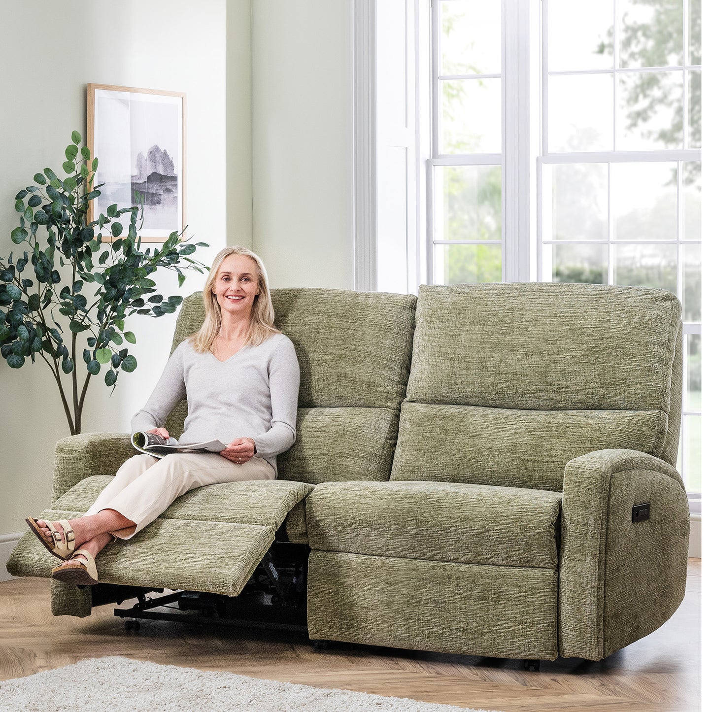 Woman sitting on a green celebrity southwell recliner sofa in a bright living room.
