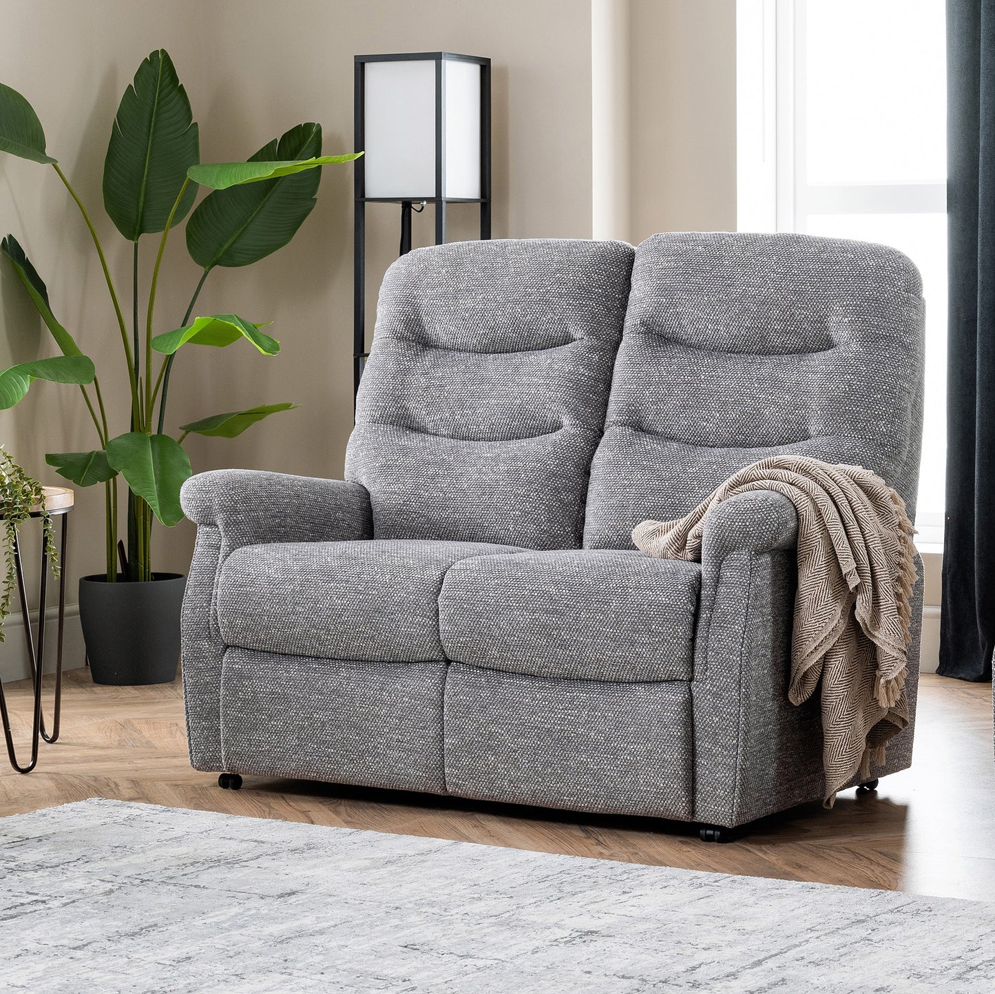 Gray recliner chair in a living room setting with a plant and lamp in the background.