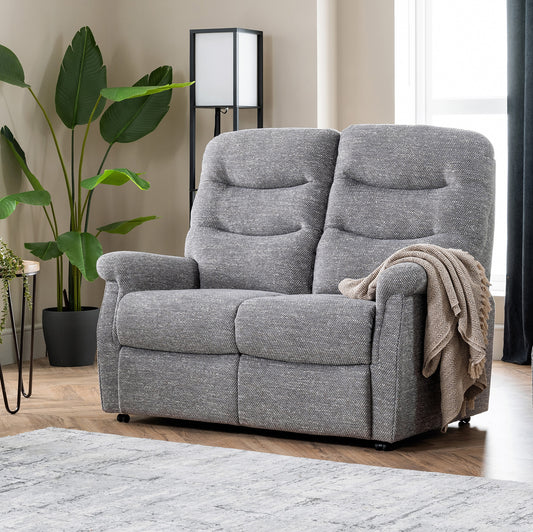Gray recliner chair in a living room setting with a plant and lamp in the background.