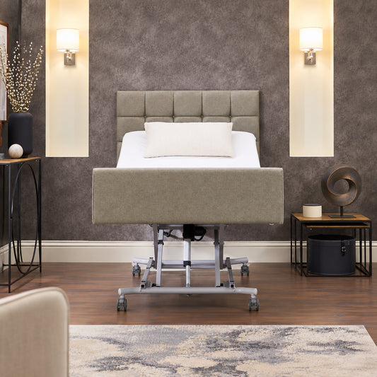 A mid-height adjustable hospital-style bed frame with a tufted headboard and upholstered side rails, shown raised on a wheeled metal base in a staged bedroom setting with wood flooring, wall sconces, side tables, and a rug.