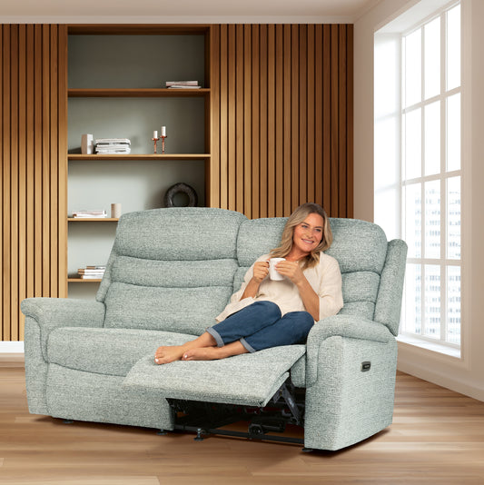 Woman sitting on a gray recliner in a living room with wooden floor and bookshelf.